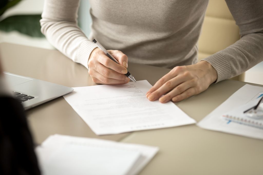 Women signing name on a piece of paper on a desk